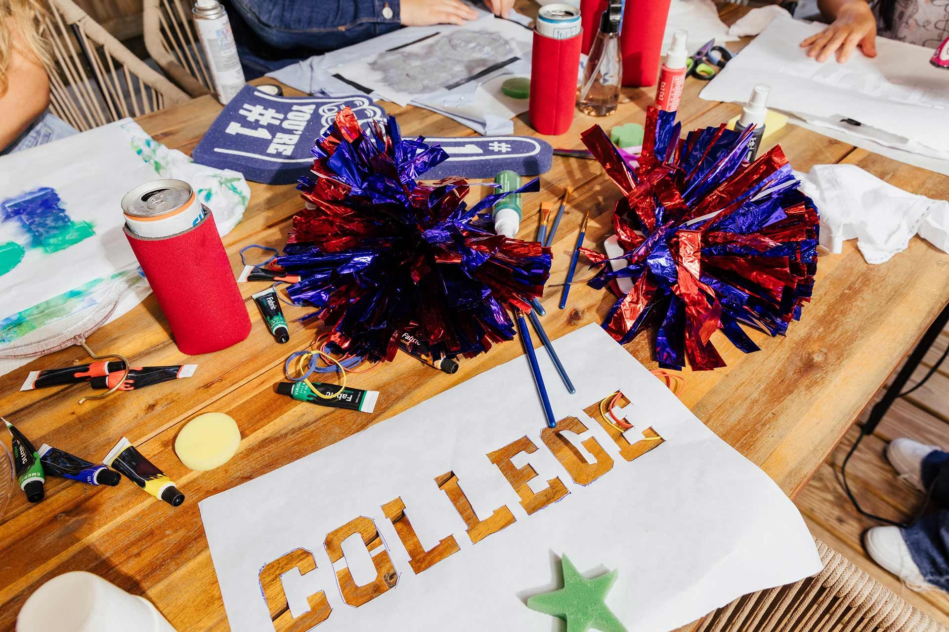 College stencil and pom poms on a table around friends at a game day craft party